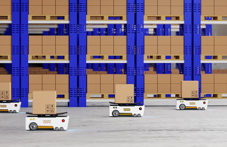 Three white mobile robots with boxes on top of them navigating an aisle with blue racks. 