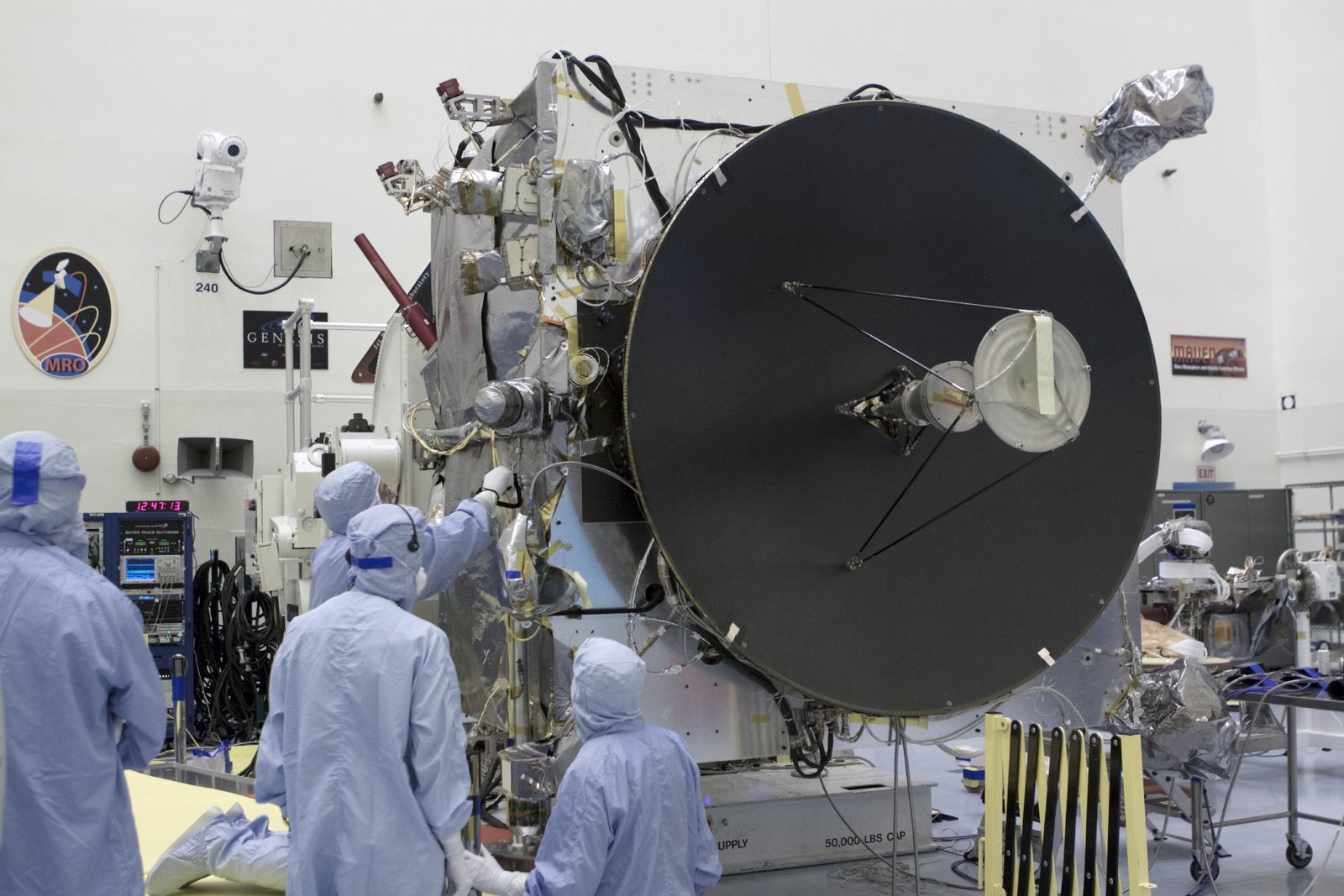 Technicians in cleanroom fits work on a spacecraft with a spacious dish-formed antenna in a laboratory setting