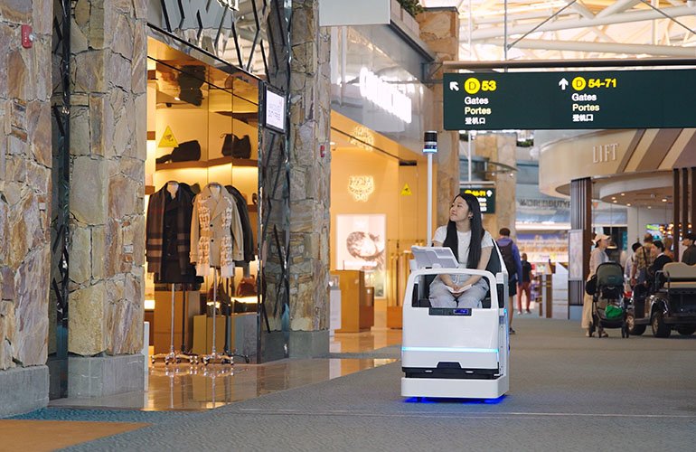 A girl with long dark hair riding in an A&K Robotics' mobility pod in an airport. 