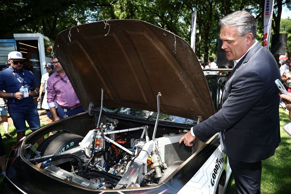 a man talking while pointing to the under hood of an open car