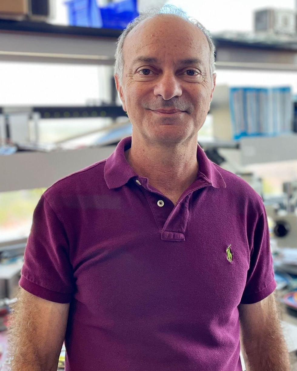 an older man in an eggplant colored polo shirt posing for a portrait