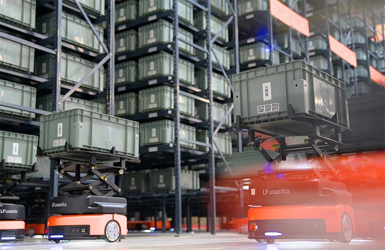 Two orange mobile robots from Quicktron Robotics carrying grey totes through a warehouse with racking in the background. 