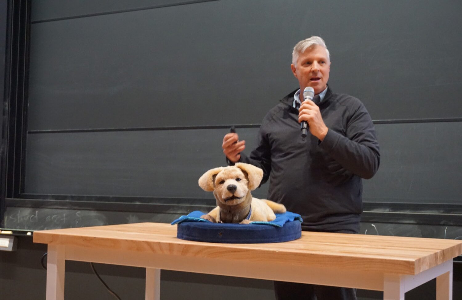 Tom Stevens standing behind a table with a tan colored robotic dog on it. 