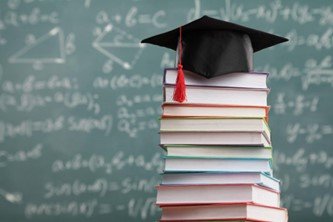 college cap and stacked books in front of chalkboard