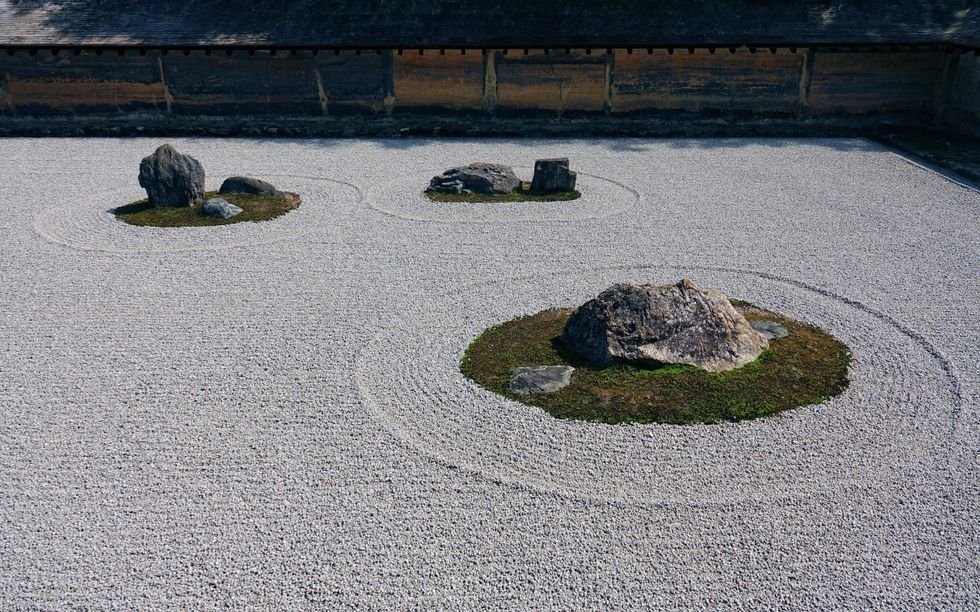 Three groups of stones surrounded by moss sit in a yard of carefully raked gravel in a Japanese temple.