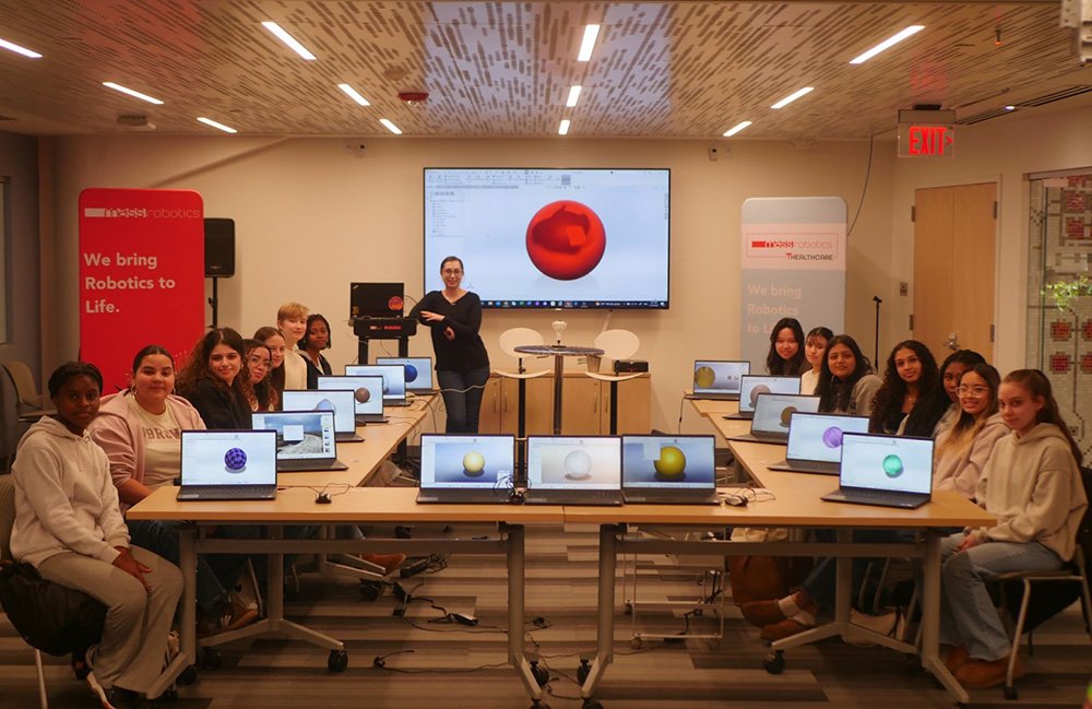 A group of teenage girls participating in MassRobotics Jumpstart Fellowship Program. The girls are all sitting at a table with laptops open. 